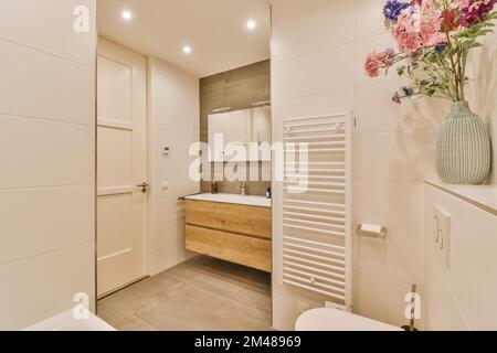 Ein modernes Badezimmer mit Blumen in der Vase und Toilettenartikeln an der Wand neben der Badewanne ist weiß Stockfoto