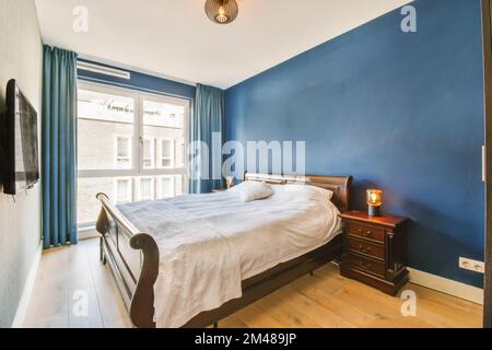Ein Schlafzimmer mit blauen Wänden und Holzfußboden, einschließlich eines großen Bettes in der Mitte des Zimmers ist eine kleine HolzKommode Stockfoto
