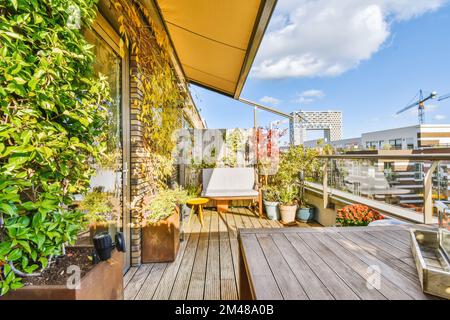 Ein Balkon mit Pflanzen und Töpfen auf der Holzterrasse vor einem Apartmentgebäude unter Baukränen ist im sichtbar Stockfoto