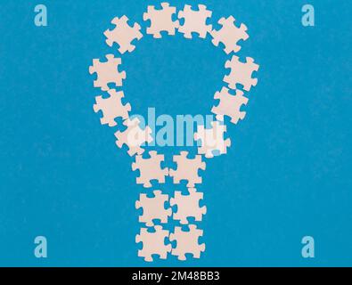 Weiße Puzzles in Form einer Glühbirne auf blauem Hintergrund, flach liegend. Stockfoto