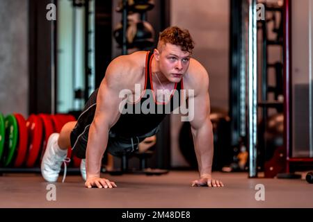 Ein junger Sportler macht Liegestütze auf dem Boden im Fitnessstudio Stockfoto