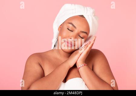 Schönheitsschlafkonzept. Porträt von schwarzer Körper-positiver Frau, die vor pinkem Studiohintergrund schläft Stockfoto