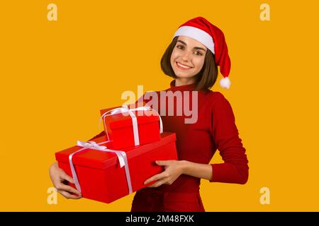 Fröhliche junge brünette Frau in Weihnachtsmann-Hut mit Weihnachtsgeschenken Stockfoto