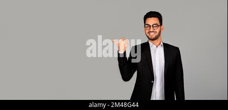 Ein gut aussehender, lächelnder arabischer Geschäftsmann im Anzug, der in den Kopierraum zeigt Stockfoto
