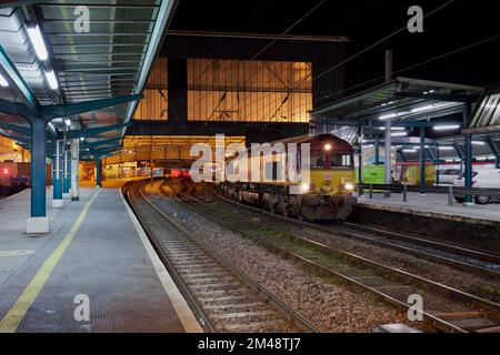 EWS-Aufmachung DB Cargo Rail UK Klasse 66 Lokomotive 66065 am Bahnhof Carlisle mit einem Güterzug mit Stahlstange Stockfoto