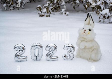 Weißes, flauschiges Hasenspielzeug mit silbernen Zahlen 2023 auf weißem Schneewald-Hintergrund. Speicherplatz kopieren. Symbol des chinesischen Neujahrs 2023. Stockfoto