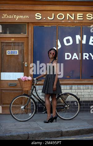 Mädchen steht mit Fahrrad vor dem alten Laden in der Colombia Road, Flower Market, East London, Großbritannien Stockfoto