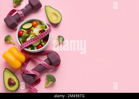 Schüssel mit Gemüsesalat, Kurzhanteln und Maßband auf farbigem Hintergrund Stockfoto