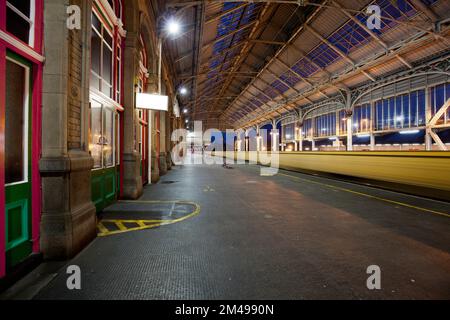 Güterzug, der durch den Bahnhof Preston fährt, mit Bewegungsunschärfe neben einem leeren Bahnsteig. Stockfoto