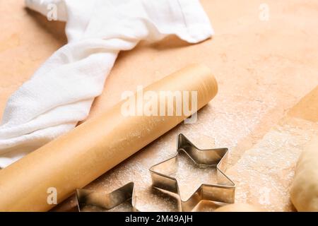 Rolle Backpapier und Keksschneider auf beigefarbenem Tisch, Nahaufnahme Stockfoto