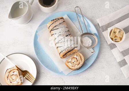 Blauer Teller mit köstlichem Schwammkuchenbrötchen, Schokolade und einer Tasse Kaffee auf einem weißen Tisch Stockfoto