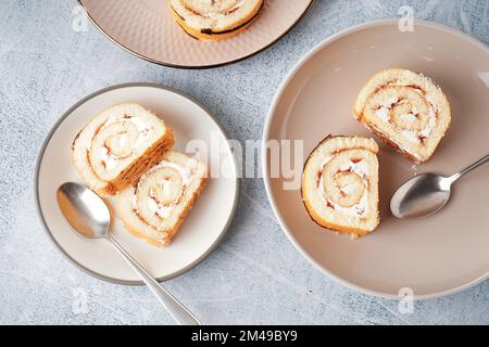 Teller mit köstlichen Kuchenrollen und Löffeln auf einem hellen Tisch Stockfoto