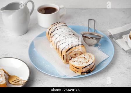 Blauer Teller mit köstlichem Schwammkuchenbrötchen und Tasse Kaffee auf weißem Tisch Stockfoto