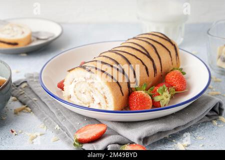 Teller mit köstlichem Schwammkuchenbrötchen und frischen Erdbeeren auf einem hellen Tisch Stockfoto