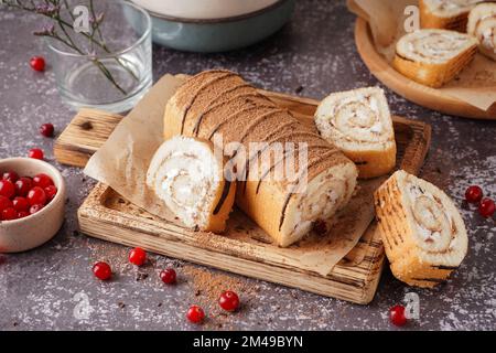 Schneidebrett mit köstlicher Schwammkuchenrolle und frischen Cranberries auf grauem Tisch Stockfoto