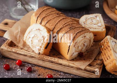 Schneidebrett mit köstlicher Schwammkuchenrolle und frischen Cranberries auf grauem Tisch Stockfoto