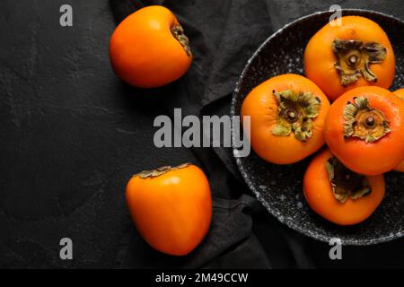 Platte mit frischen, reifen Persimonen auf dunklem Hintergrund Stockfoto
