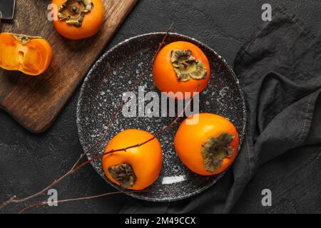 Platte mit frischen, reifen Persimonen auf dunklem Hintergrund Stockfoto