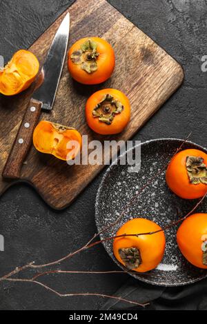 Holzbrett und -Teller mit frischen, reifen Persimonen auf dunklem Hintergrund Stockfoto