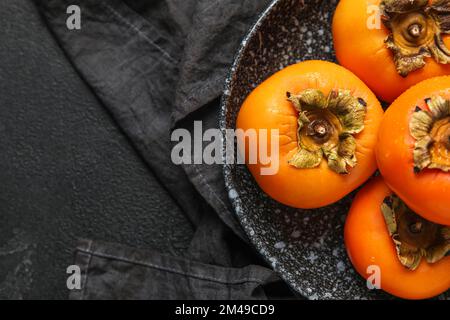 Platte mit frischen, reifen Persimonen auf dunklem Hintergrund Stockfoto