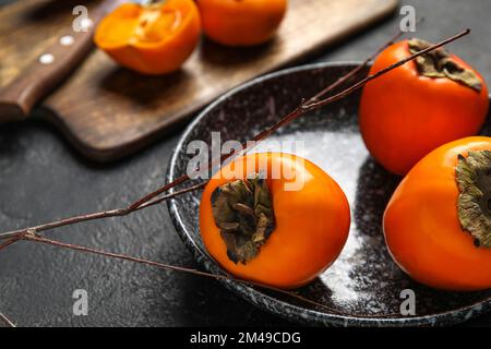 Teller mit frischen, reifen Persimonen auf dunklem Hintergrund, Nahaufnahme Stockfoto