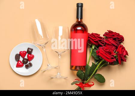 Flasche Wein, Gläser, Rosen und Süßigkeiten auf beigefarbenem Hintergrund. Valentinstag-Feier Stockfoto