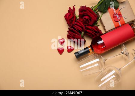Flasche Wein, Gläser, Süßigkeiten und Rosen auf beigefarbenem Hintergrund. Valentinstag-Feier Stockfoto