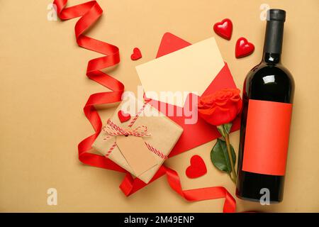 Leerer Brief mit Rose, Flasche Wein, Geschenk und Herzen auf beigefarbenem Hintergrund. Valentinstag-Feier Stockfoto