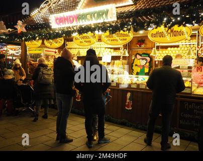 Nachtsicht auf die Süßwarenfabrik, einen Süßwarenstand auf dem Weihnachtsmarkt und Menschen, die davor in Deutschland stehen Stockfoto