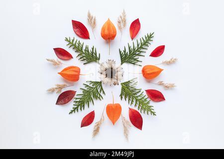 Mandala-Muster aus orangefarbenen Herbstblättern, Blumen, grüne Äste auf weißem Hintergrund Stockfoto