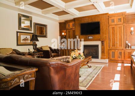 Braunes Ledersofa und Sessel im Wohnzimmer mit Kassettendecke innen üppig dekoriertes und luxuriöses Haus im Cottage-Stil. Stockfoto