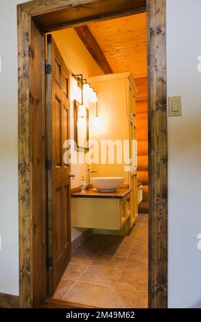 Weißes Waschbecken auf Kosmetikbereich im Hauptbadezimmer mit braunem Keramikfliesenboden im Blockhaus. Stockfoto