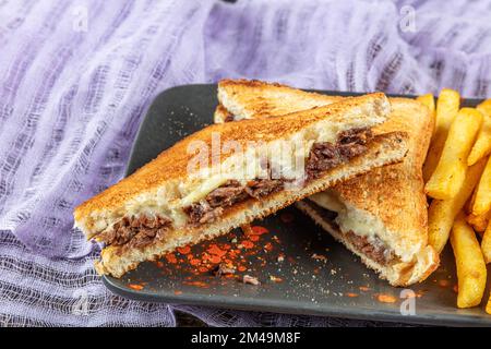 Club Toast mit Cheddar-Käse. Geschmolzener Käse, Toast, Sandwich und Roastfleisch. Gebratenes Fleisch wird mit Toast und Salat serviert. Stockfoto