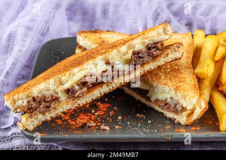 Club Toast mit Cheddar-Käse. Geschmolzener Käse, Toast, Sandwich und Roastfleisch. Gebratenes Fleisch wird mit Toast und Salat serviert. Stockfoto