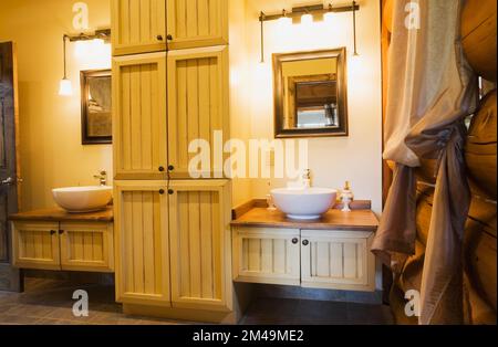 Seine und ihre weiße Schüssel sinken auf dem Waschtisch im Hauptbadezimmer mit braunem Keramikfliesenboden im Blockhaus. Stockfoto