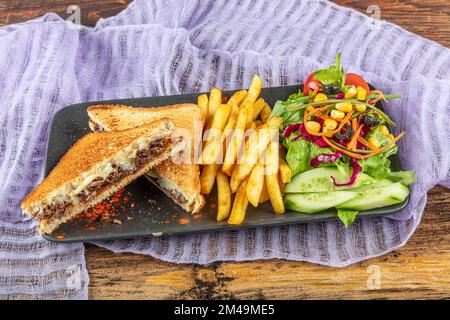 Club Toast mit Cheddar-Käse. Geschmolzener Käse, Toast, Sandwich und Roastfleisch. Gebratenes Fleisch wird mit Toast und Salat serviert. Stockfoto