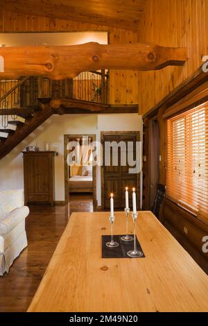 Langer hölzerner Esstisch mit brennenden Wachskerzen im Speisesaal mit braun gebeiztem und lackiertem Hartholzboden im Blockhaus. Stockfoto