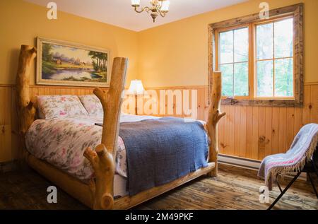 Rustikales Himmelbett im oberen Gästeschlafzimmer mit nuancierten braunen Buntböden im Blockhaus. Stockfoto