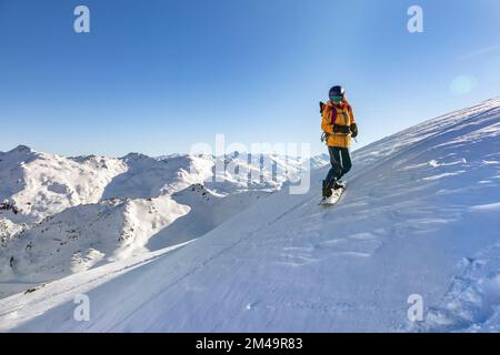 Ein junges Mädchen mit gelber Jacke und hellem dunklen Helm reitet auf einem Snowboard in den Bergen, Tirol, Alpen, Österreich Stockfoto