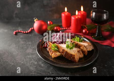 Festliche Schweinebraten mit Rotkohl auf einem dunklen Teller, rote Kerzen, Wein und Weihnachtsdekoration vor dunklem Hintergrund, Kopierbereich, ausgewählt Stockfoto