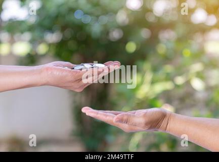 Frauenhand gibt Geldmünze, die man aus unscharfem Hintergrund zur Hand geben kann. Stockfoto
