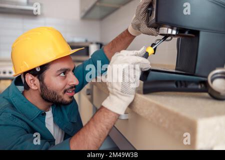 Mann mit Schraubenzieher, der eine Kaffeemaschine am Tisch in der Küche repariert. Wartungs- und Reparaturkonzept Stockfoto