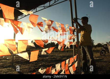 Ein Mann, der bei der Vorbereitung einer Naturschutzveranstaltung im Dorf Maubesi, Central Rote, Rote Ndao, East Nusa Tenggara, Indonesien, Linien mit kleinen dekorativen Flaggen in Rot und Weiß anlegt, die die indonesische Nationalflagge symbolisieren. Stockfoto