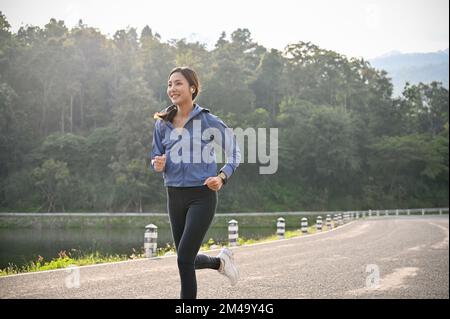 Eine glückliche und gesunde Asiatin der Millennials in Sportbekleidung, die morgens im Park gerne Musik hört. Stockfoto