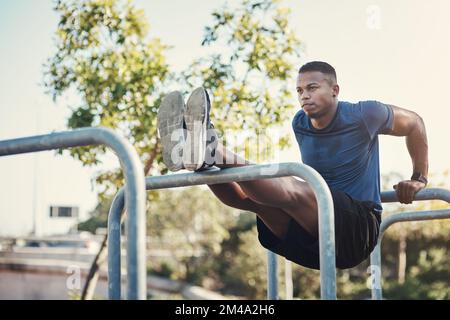 Ich arbeite an den Trizeps. Aufnahme eines gutaussehenden jungen Mannes in voller Länge, der Dips macht, während er draußen in einem Calisthenics-Park trainiert. Stockfoto