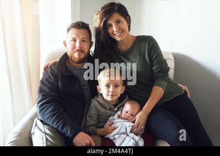 Wir haben einander und das ist alles, was zählt. Porträt einer fröhlichen jungen Familie, die tagsüber zusammen auf einem Sofa zu Hause sitzt. Stockfoto