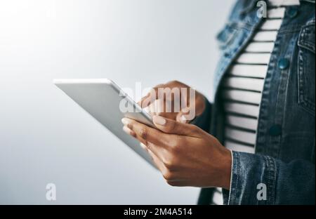 Von überall aus verbinden. Studioaufnahme einer unbekannten jungen Frau, die ihr digitales Tablet vor grauem Hintergrund verwendet. Stockfoto