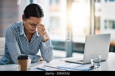 Ich kann nur an das Ende dieses Tages denken. Eine junge Geschäftsfrau, die gestresst aussieht, während sie in einem Büro arbeitet. Stockfoto