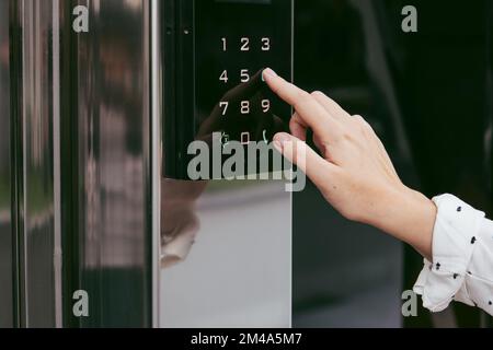 Die Hand einer Frau, die eine Sprechanlage am Eingang des Gebäudes benutzt. Mit einem elektronischen Schloss Stockfoto