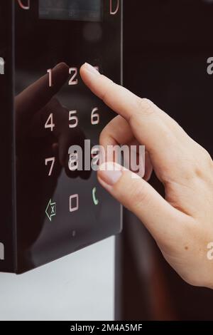 Die Hand einer Frau, die eine Sprechanlage am Eingang des Gebäudes benutzt. Mit einem elektronischen Schloss Stockfoto